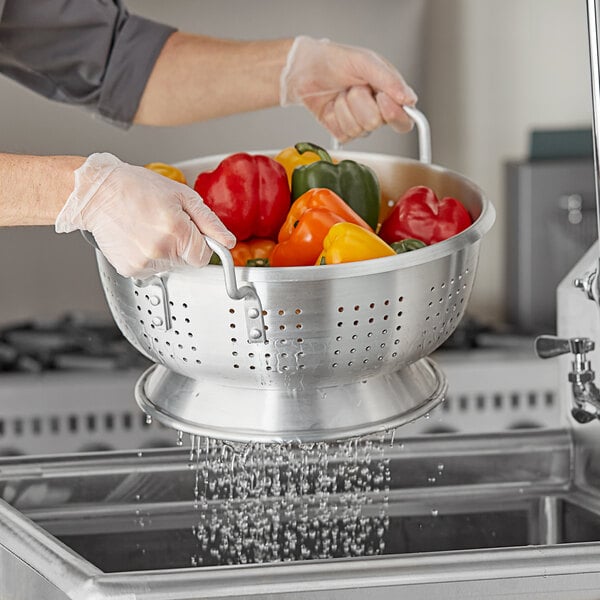 A person holding a Choice heavy-duty aluminum colander full of peppers.