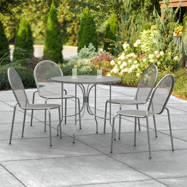 A Lancaster Table & Seating Harbor Gray round outdoor table with ornate legs and four chairs on a patio.