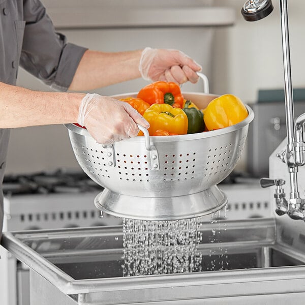 A man using a Choice heavy-duty aluminum colander to wash yellow bell peppers.