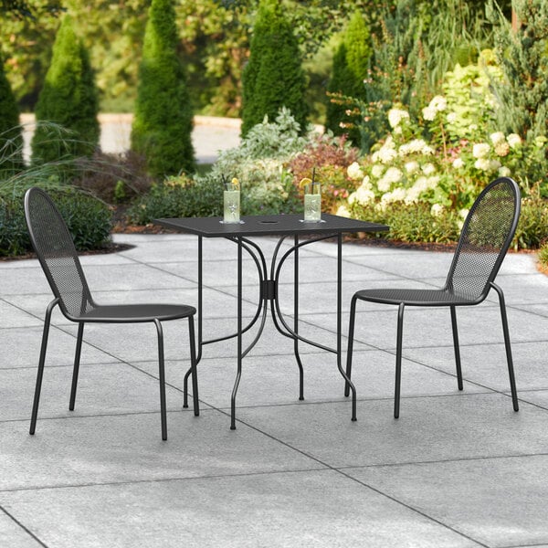 A Lancaster Table & Seating rectangular black outdoor table with two chairs on a patio.