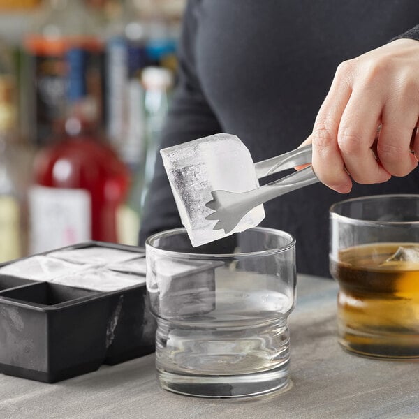 A person using a Choice Black Silicone 2" Cube Ice Mold to add ice to a glass of liquid.