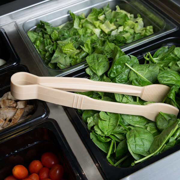 Thunder Group beige tongs in a bowl of spinach at a salad bar.