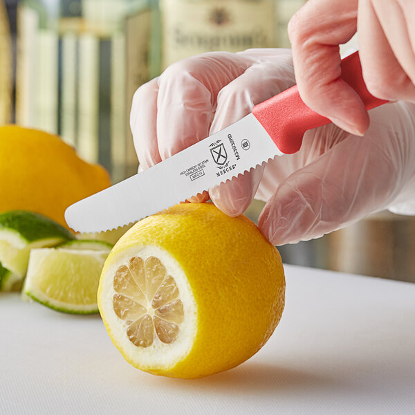 A person using a Mercer Culinary red rounded tip paring knife to cut a lemon.