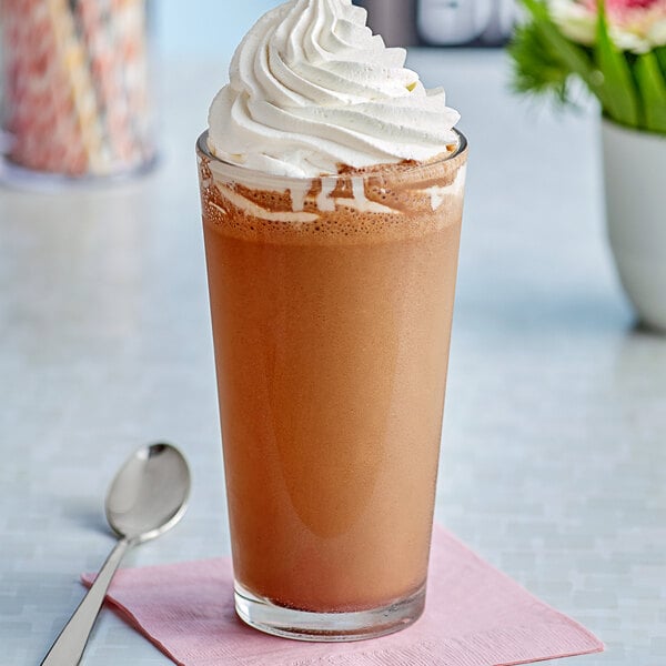 A glass of brown liquid with whipped cream on top.