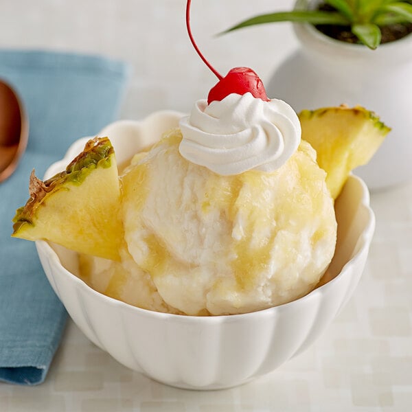 A bowl of ice cream with J. Hungerford Smith pineapple topping, a cherry, and whipped cream on top.