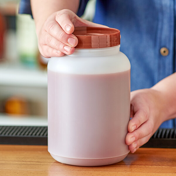 A person holding a Choice plastic container with a brown lid filled with pink liquid.