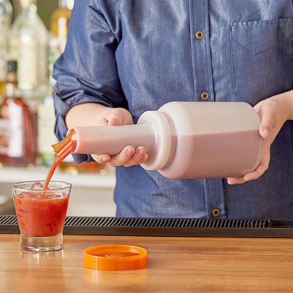 A person pouring red liquid from a Choice pour bottle with an orange cap into a glass.