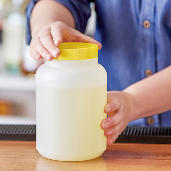 A person holding a plastic container with a yellow lid full of liquid.