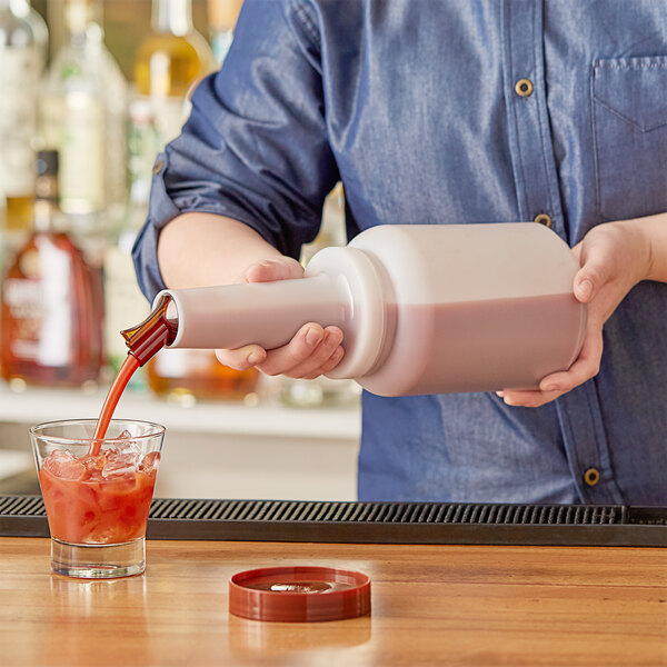 A person using a Choice pour bottle with a brown spout to pour liquid into a glass with a straw.