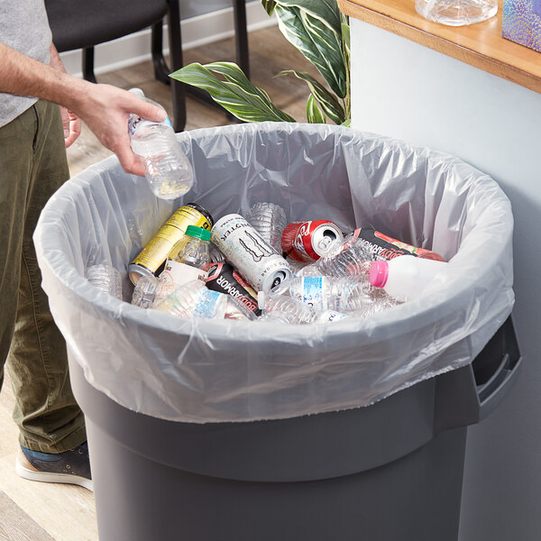 A man putting plastic bottles into a clear Lavex trash bag inside a trash can.