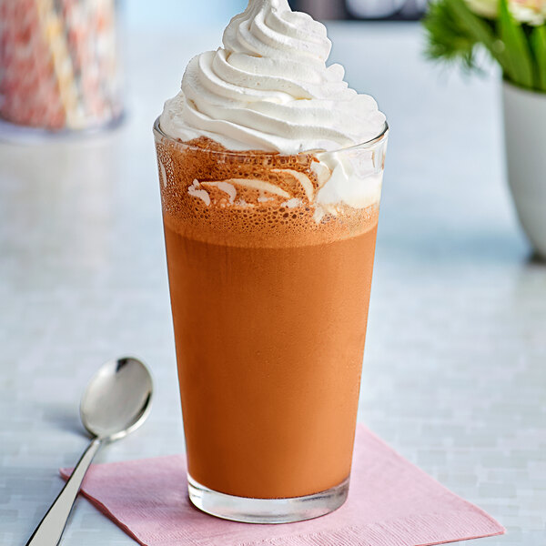 A glass of brown liquid with whipped cream on top.
