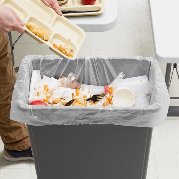 A person holding a tray of food in a trash can lined with a Lavex Hercules clear trash bag.