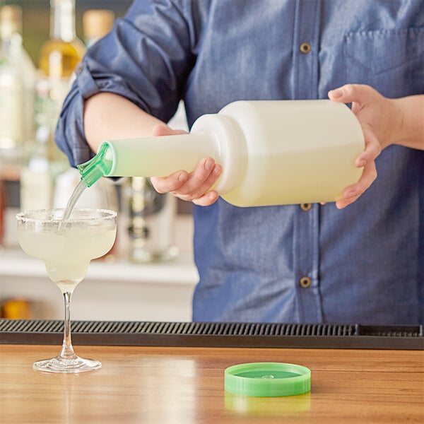A person using a Choice green plastic pour bottle to pour a drink into a glass on a bar counter.