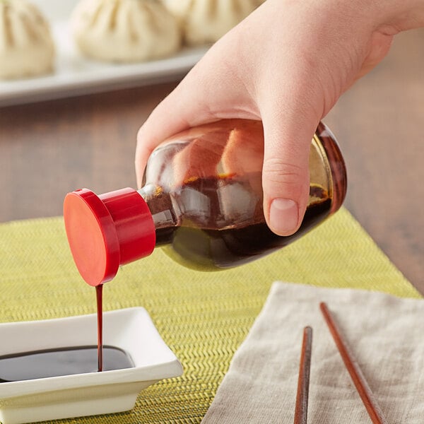 A blurry close up of a person's hand pouring Town Round Red Top Soy Sauce from a bottle into a bowl of dumplings.
