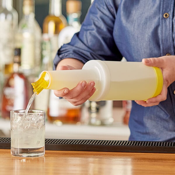 A person pouring liquid from a white Choice bottle with a yellow spout into a glass with ice.