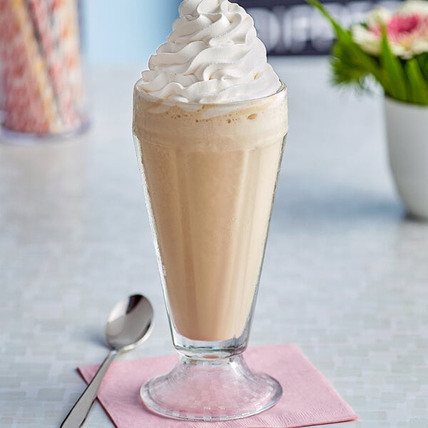 A glass of J. Hungerford Smith Vanilla milkshake with whipped cream and a spoon.