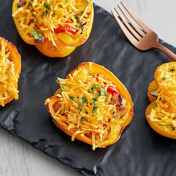 A stuffed yellow bell pepper with Violife Just Like Cheddar cheese and tomatoes on a black plate with a fork.