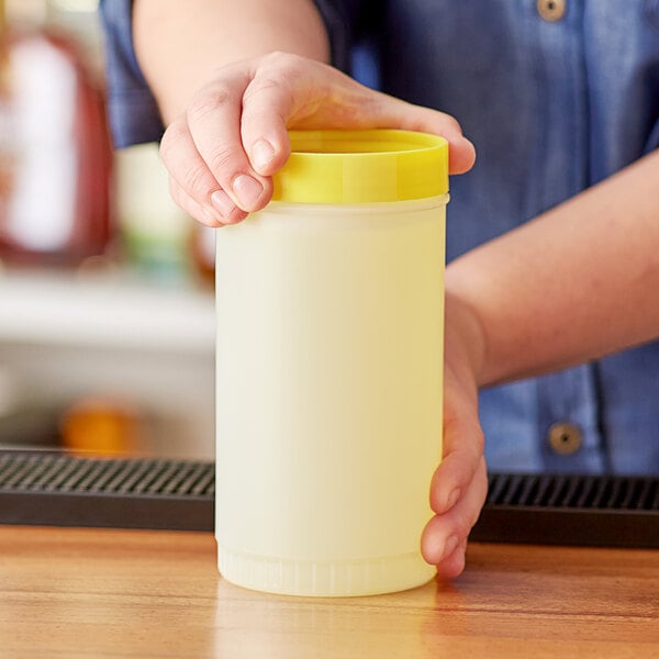 A person holding a plastic container with a yellow lid on a bar counter.