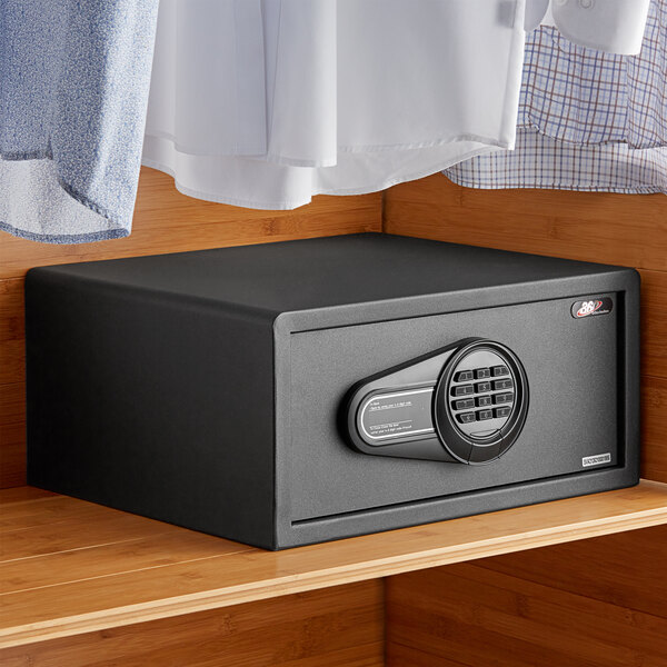 A black steel 360 Office Furniture hotel safe with electronic keypad lock on a wooden shelf.