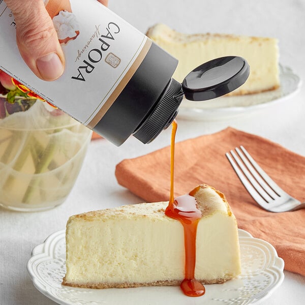 A hand pouring Capora Pumpkin Pie Flavoring Sauce onto a slice of cheesecake.