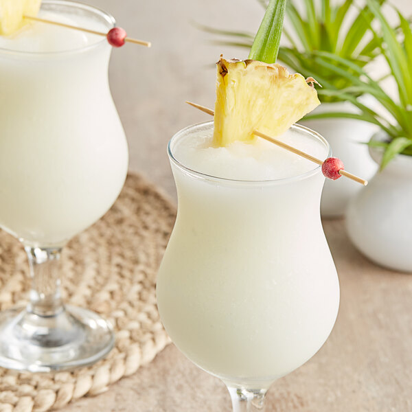 Two glasses of Coco Lopez drinks with pineapple garnish.