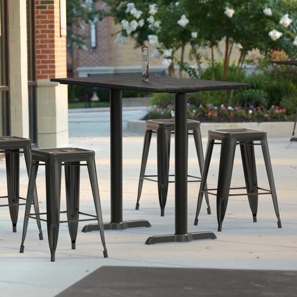 A Lancaster Table & Seating rectangular counter height table with black metal end bases and chairs outside on a patio.