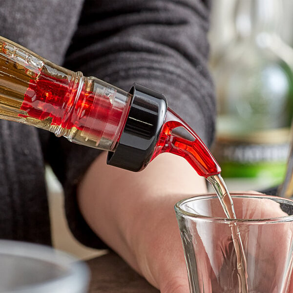 A person using a TableCraft Red Measured Liquor Pourer to pour liquid into a glass on a counter.