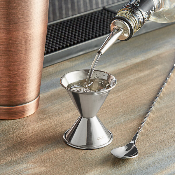 A Tablecraft stainless steel jigger being used to pour liquid into a metal cup.