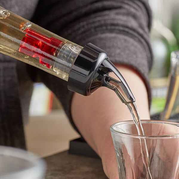 A person using a TableCraft Proper Pour measured liquor spout to pour liquid into a glass on a counter.