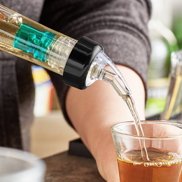 A person using a TableCraft green tail liquor pourer to pour brown liquid into a glass.