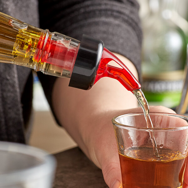 A person using a TableCraft red and yellow liquor pourer to measure and pour alcohol into a glass.