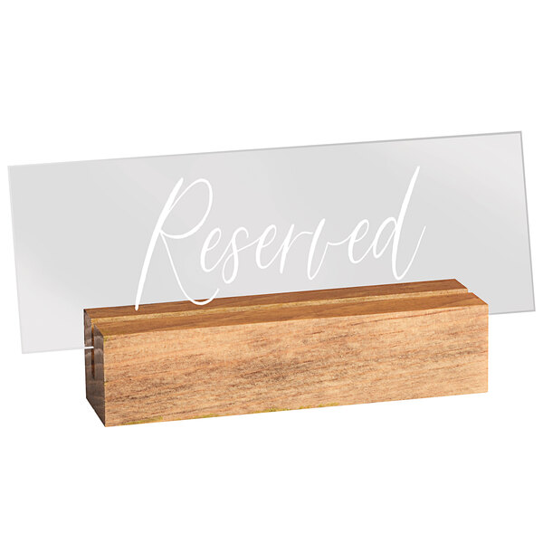 A clear acrylic sign holder on a wood block with a clear sign that says "Reserved" in white letters.