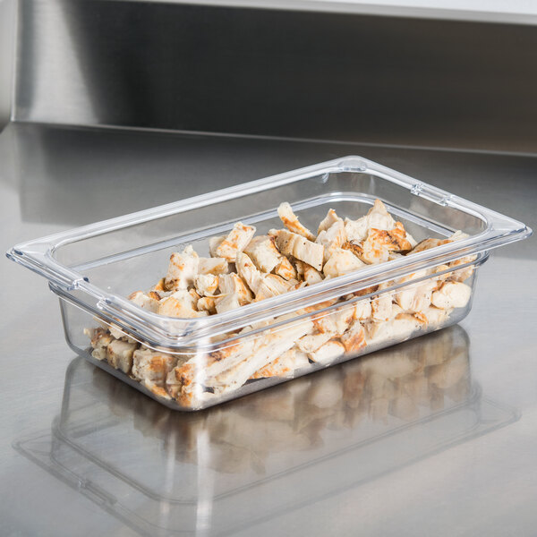A clear Carlisle plastic food pan filled with food on a counter.