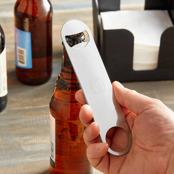 A hand holding a silver Tablecraft bottle opener.