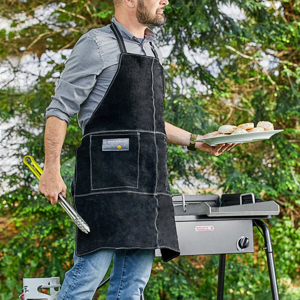 A man wearing an Outset black suede leather grill apron holding a plate of food.