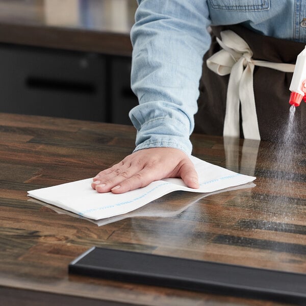 A person cleaning a table in a professional kitchen with a WypAll X70 foodservice wiper.