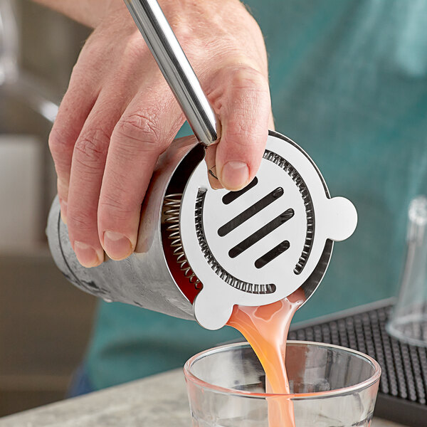 A person using a Tablecraft stainless steel cocktail strainer to pour a drink.
