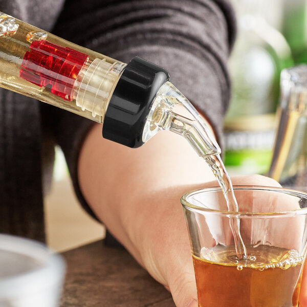 A person using a TableCraft clear spout liquor pourer to fill a shot glass.