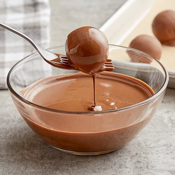 A spoon with Callebaut milk chocolate callets being dipped into a bowl of liquid chocolate.