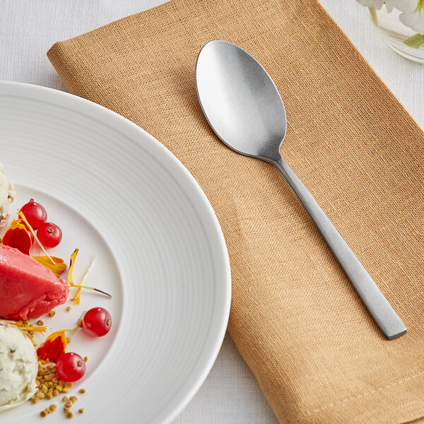 An Acopa Petra stainless steel teaspoon on a white plate with food and a napkin.