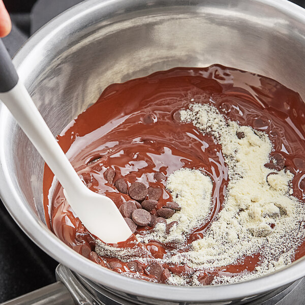 A white spoon stirring Cacao Barry powdered cocoa butter into chocolate in a bowl.