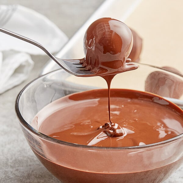 A spoon dipping into a bowl of Callebaut dark chocolate liquid.