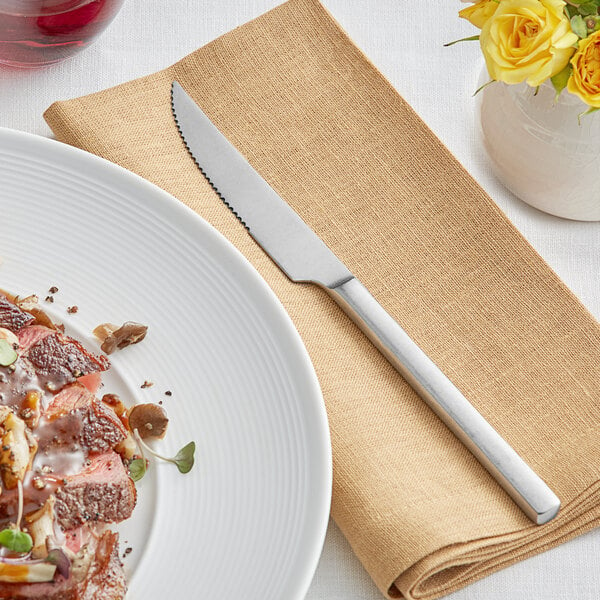 A plate of meat and mushrooms on a napkin next to an Acopa stainless steel steak knife.