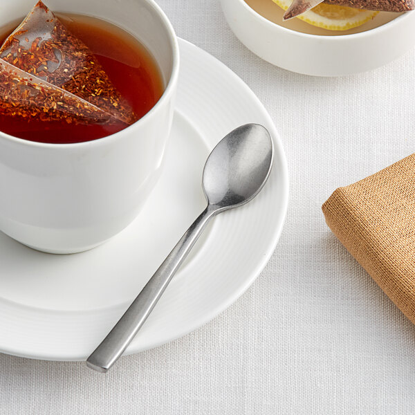 A white cup of tea with a spoon on a plate.