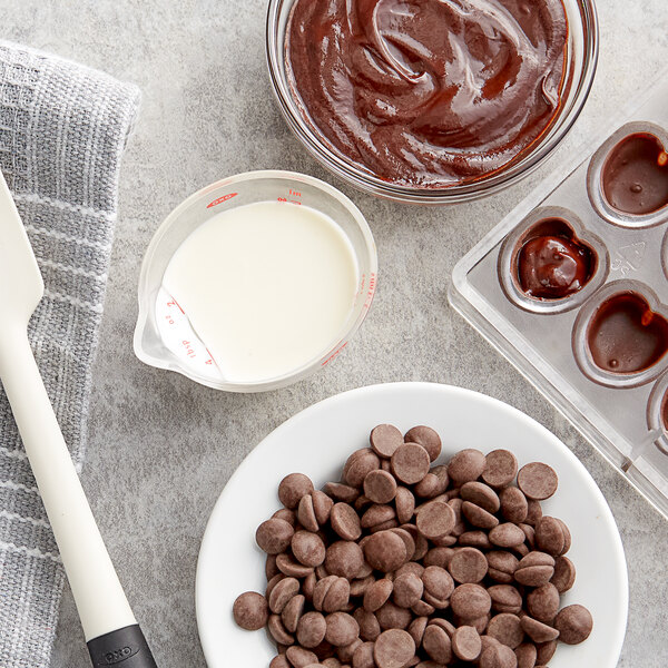 A bowl of Callebaut dark chocolate chips on a table with a bowl of milk and a plate of chocolate chips.