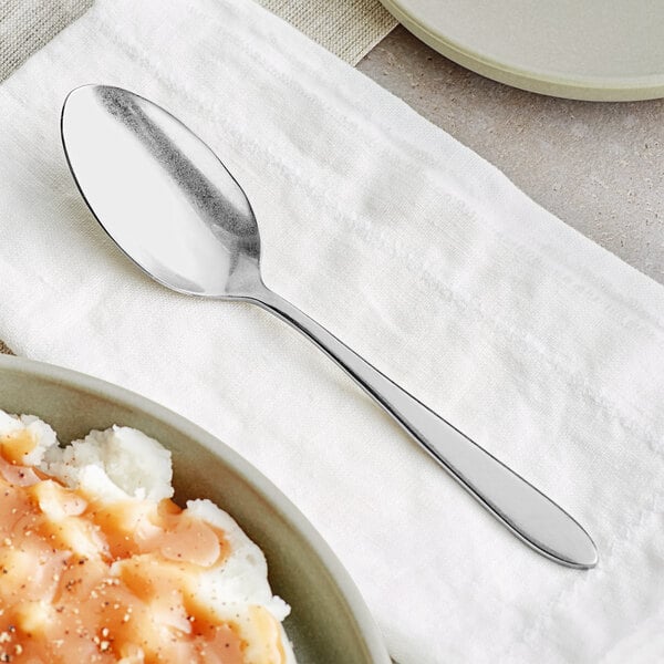 A spoon next to a bowl of mashed potatoes and gravy.