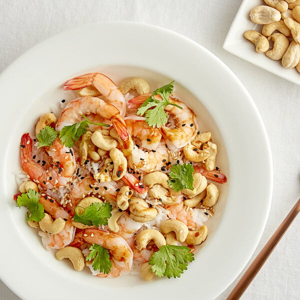 A bowl of food with shrimp and large raw cashews.