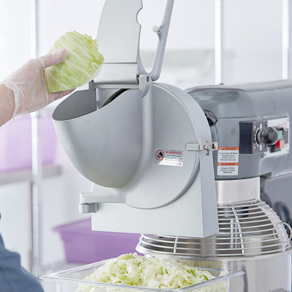 A hand holding a piece of cabbage being sliced by a Slicer Attachment on a mixer