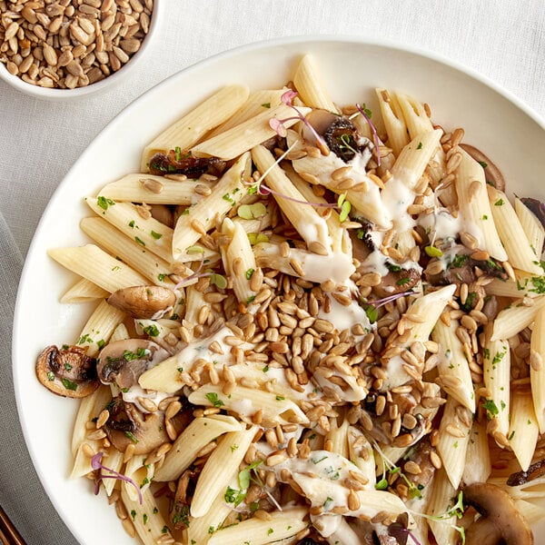 A white plate of pasta with mushrooms and Roasted Salted Sunflower Seeds.
