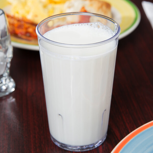 A close up of a GET Clear SAN Plastic tumbler filled with milk on a table.